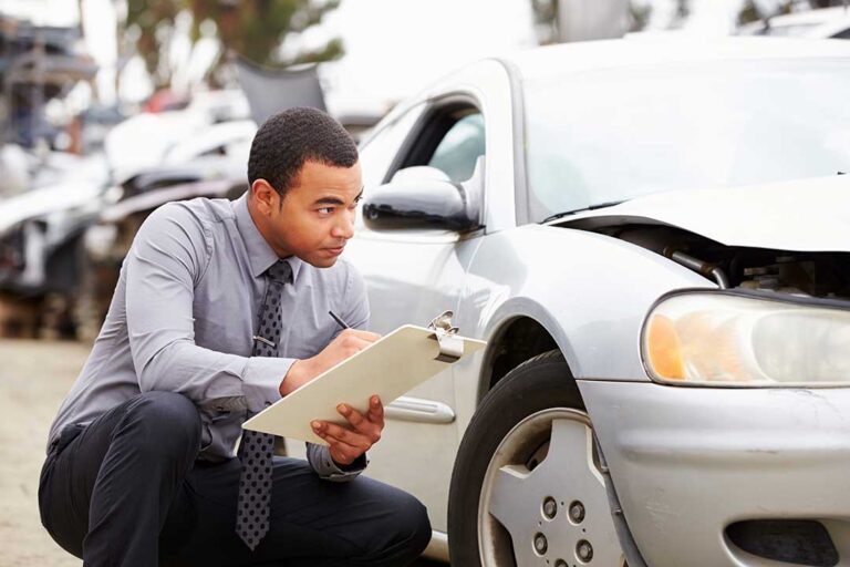 A driver reviews auto insurance documents beside a damaged vehicle after a collision.